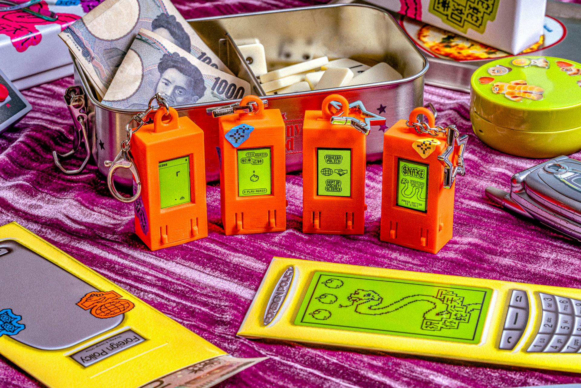 A table covered in a hongbao envelope designed in the style of a retro phone, and a row of orange mini devices displaying a game of Snake
