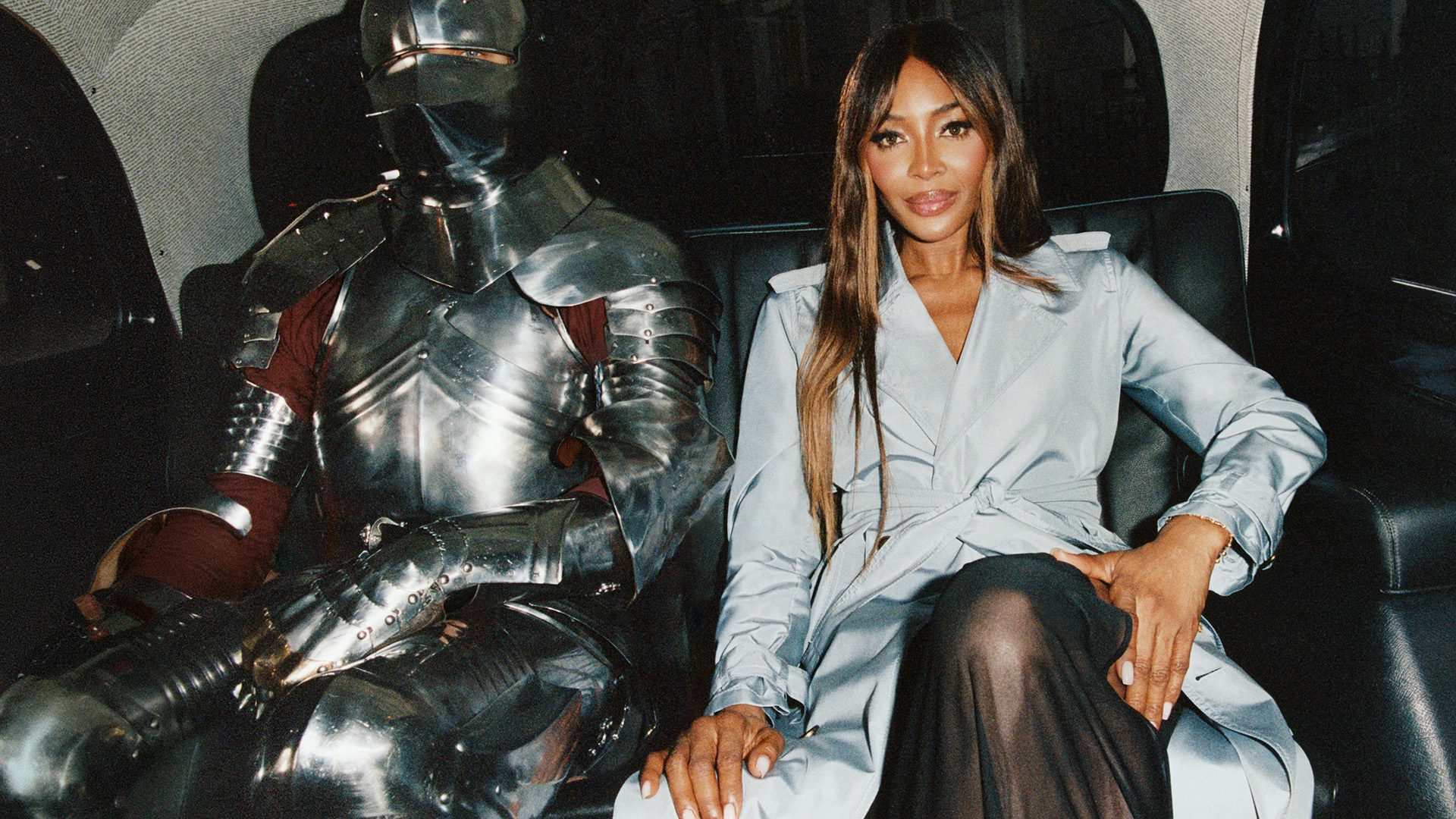 Still from Burberry's London in Love campaign featuring model Naomi Campbell in a light blue trench sat next to a knight in full armour