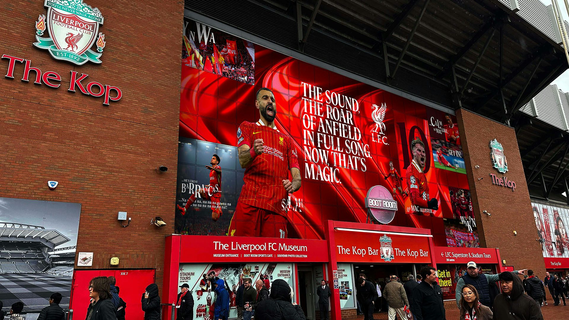 Liverpool branding shown on a stadium wrap outside Anfield that reads 'the sound the roar of anfield in full song. now that's magic'