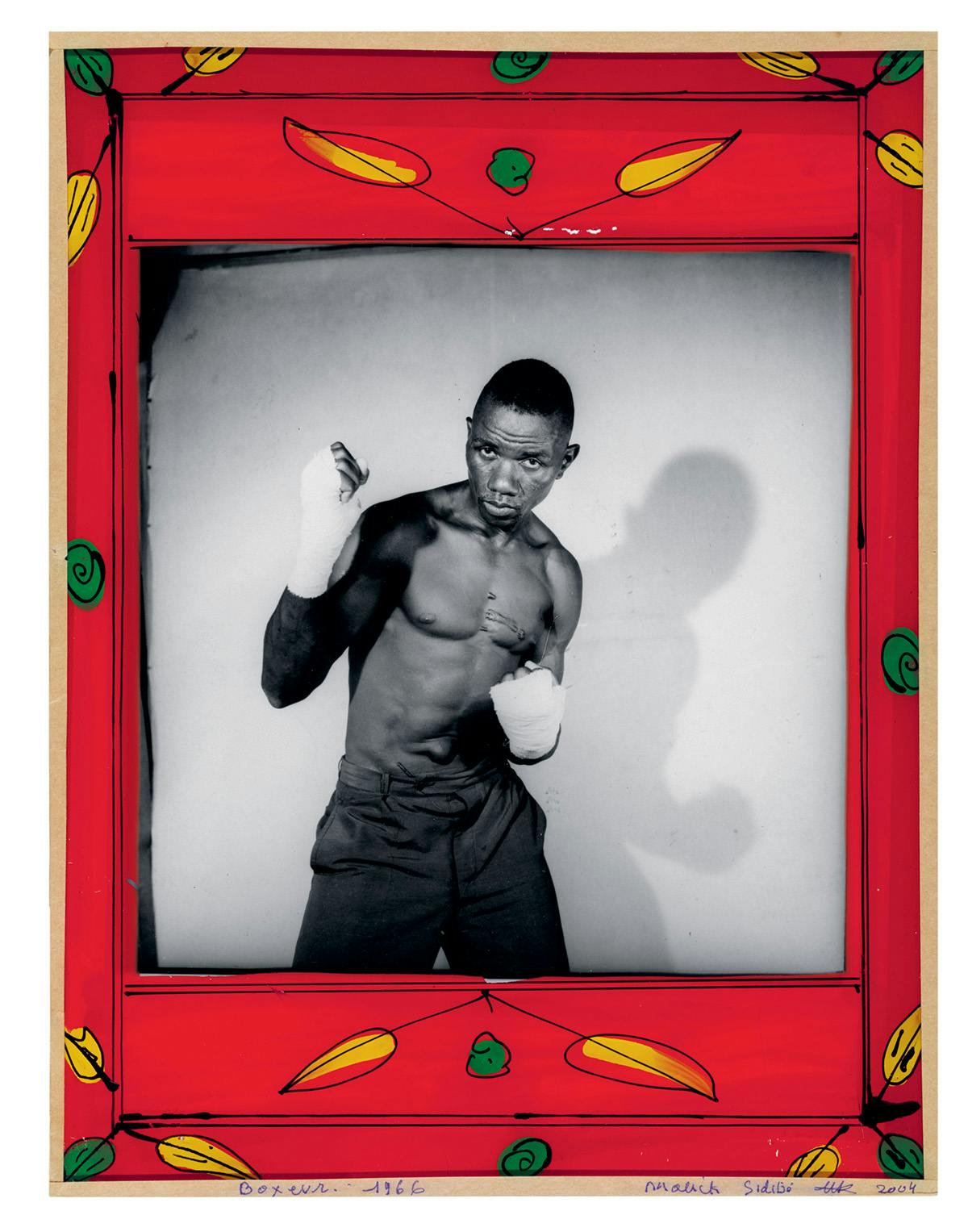 Black and white photo of a person in a boxing pose in a studio, which is bordered by a red painted frame