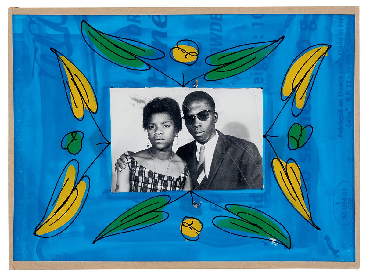 Black and white portrait of two people posing a studio, which is bordered by a blue, yellow and green painted frame