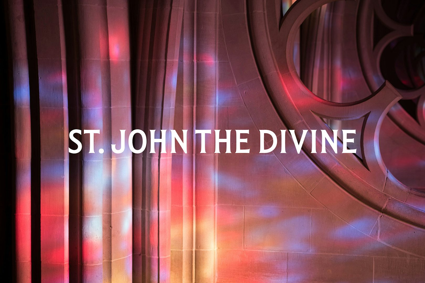 Pink light patterns cast on the interior of a cathedral wall with the wordmark 'St John the Divine' laid over it