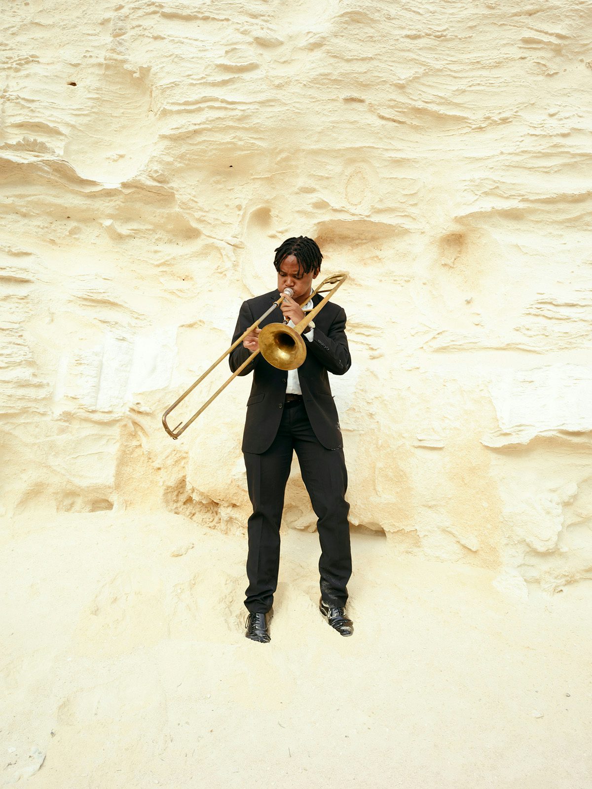 Photo by Thero Makepe of a man in a suit playing a trombone in front of a rocky wall