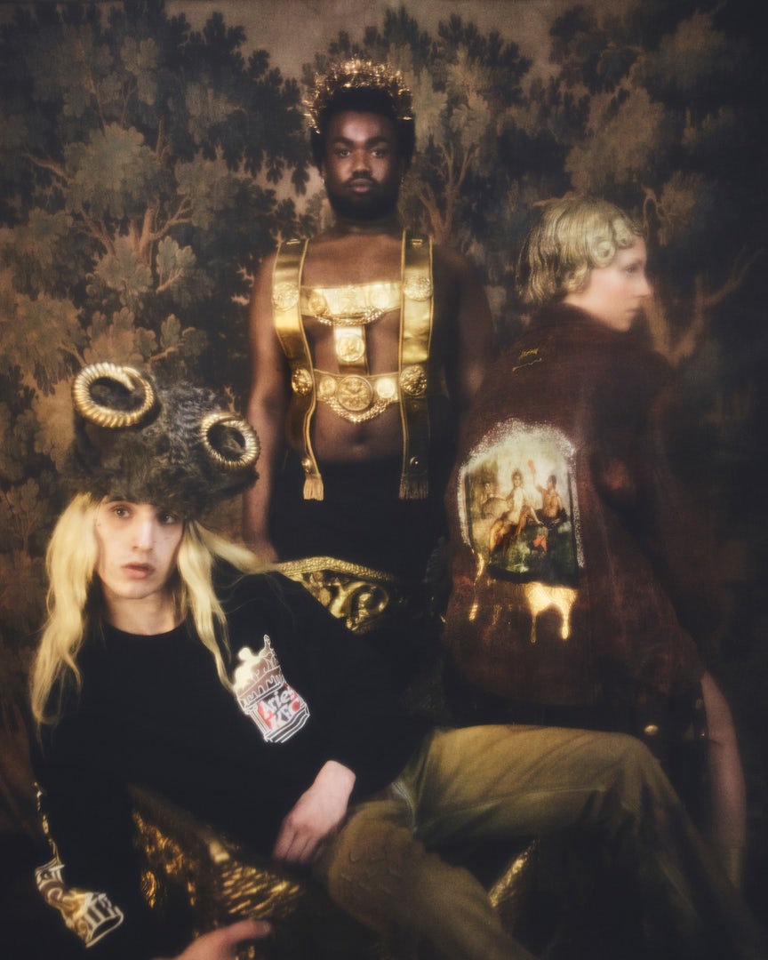 Soft focus photo of three people wearing a mix of golden armour and headwear and tops and jackets featuring the Aries and KFC branding