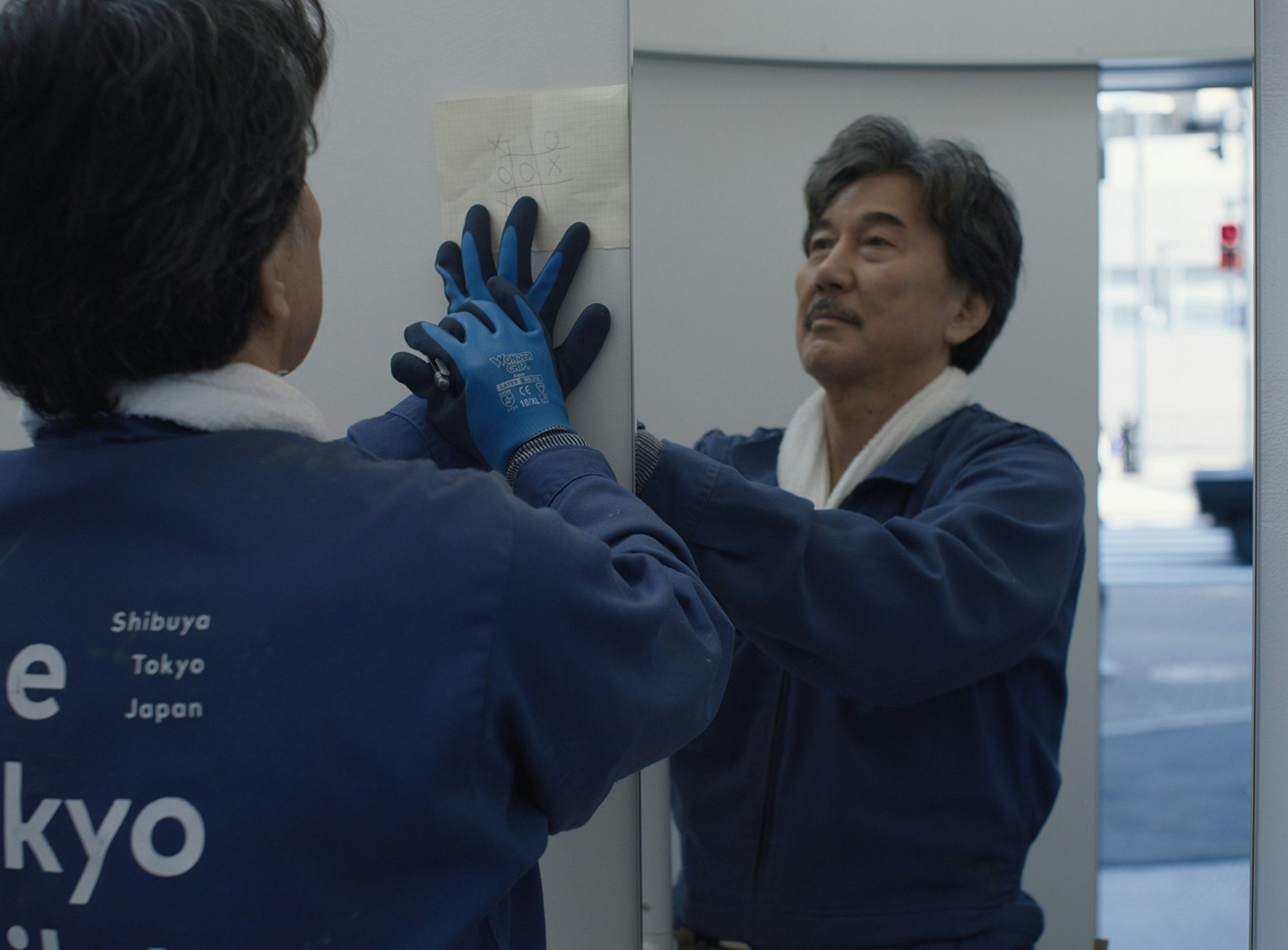 Film still from Perfect Days showing the main character Hirayama doing noughts and crosses on a piece of paper in a public restroom