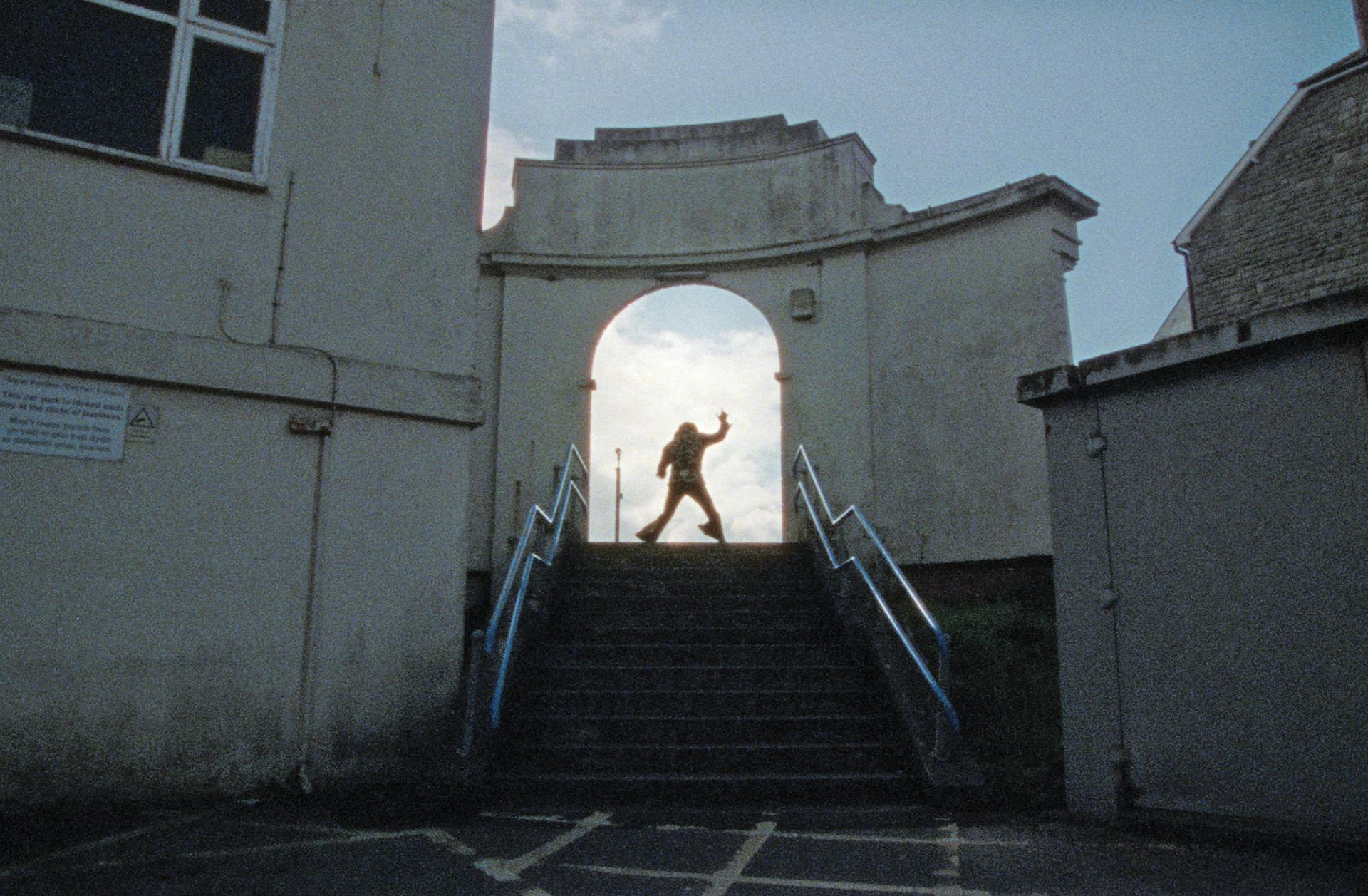 Still from the short documentary If I Can Dream by Luis Cross showing the silhouette of an Elvis impersonator posing at the top of a set of steps underneath an archway