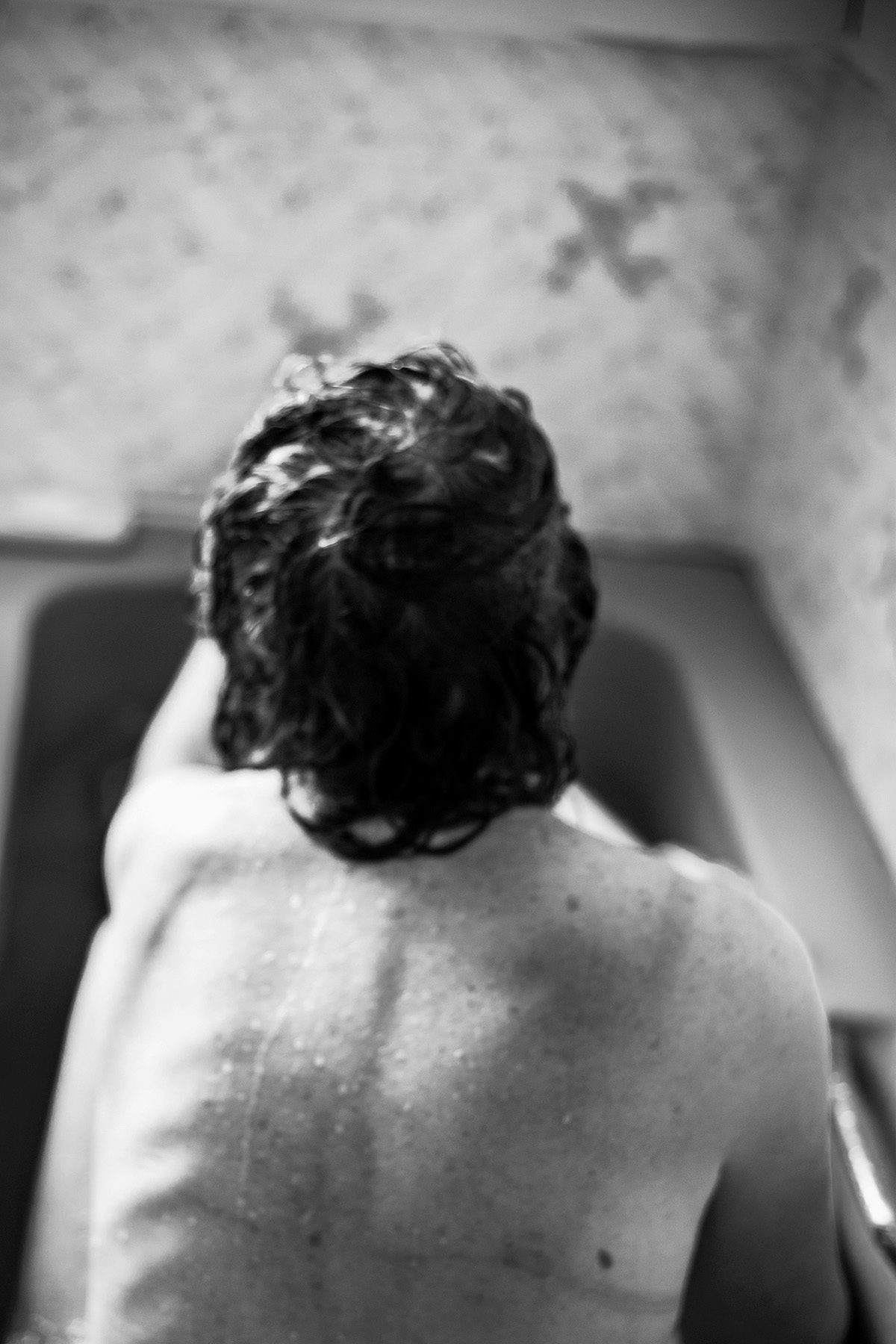 Black and white photo of a person's back facing the camera while sat in the bath
