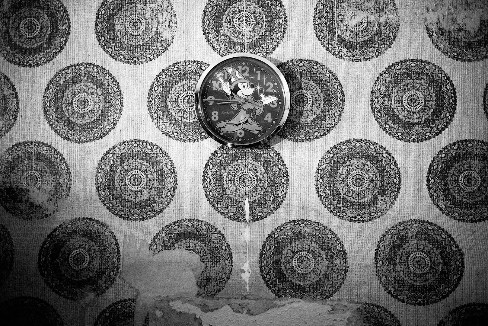 Black and white photo of a circular Mickey Mouse clock on a wall covered in circle patterned wallpaper