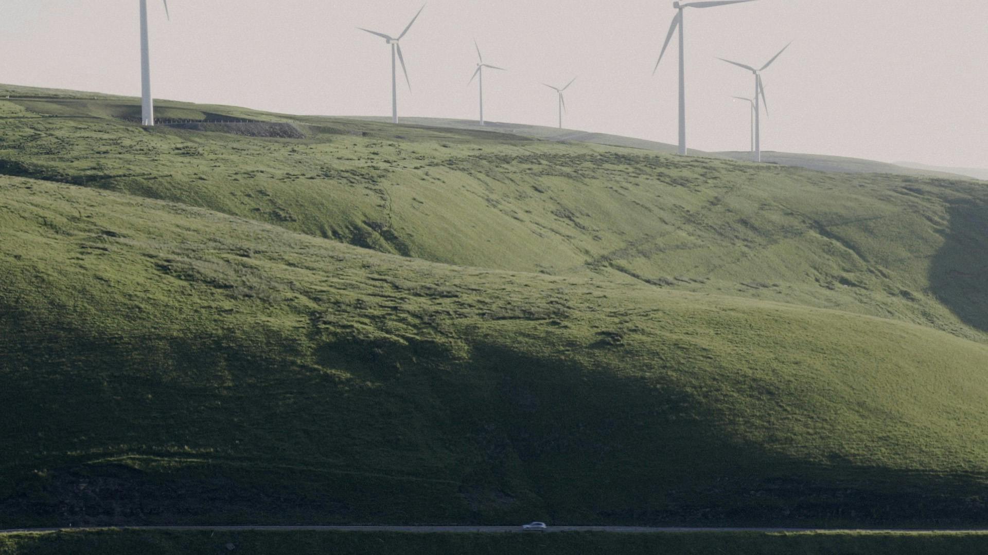 Maesteg film still showing a car driving along a road with a hillside covered in wind turbines in the background