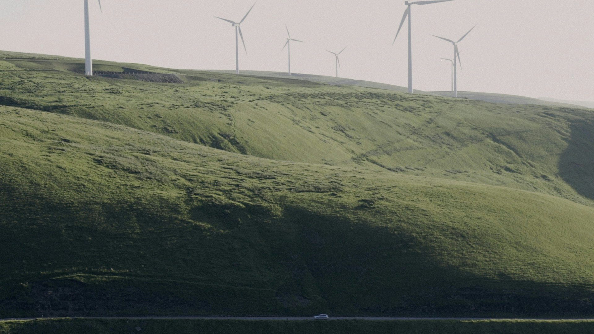 Maesteg film still showing a car driving along a road with a hillside covered in wind turbines in the background