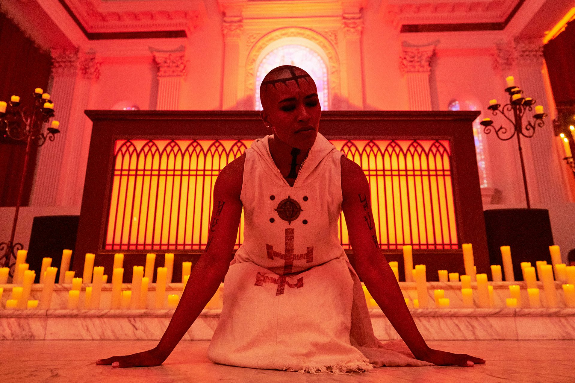 Performer in a white robe kneeling in front of a candle lit altar at Diablo IV event by Studio Secret Cinema