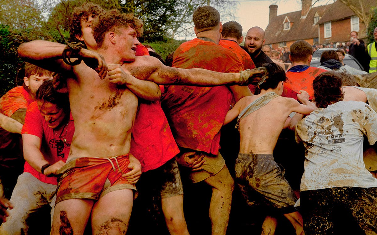 Young men in shorts covered in mud while tussling in a crowd