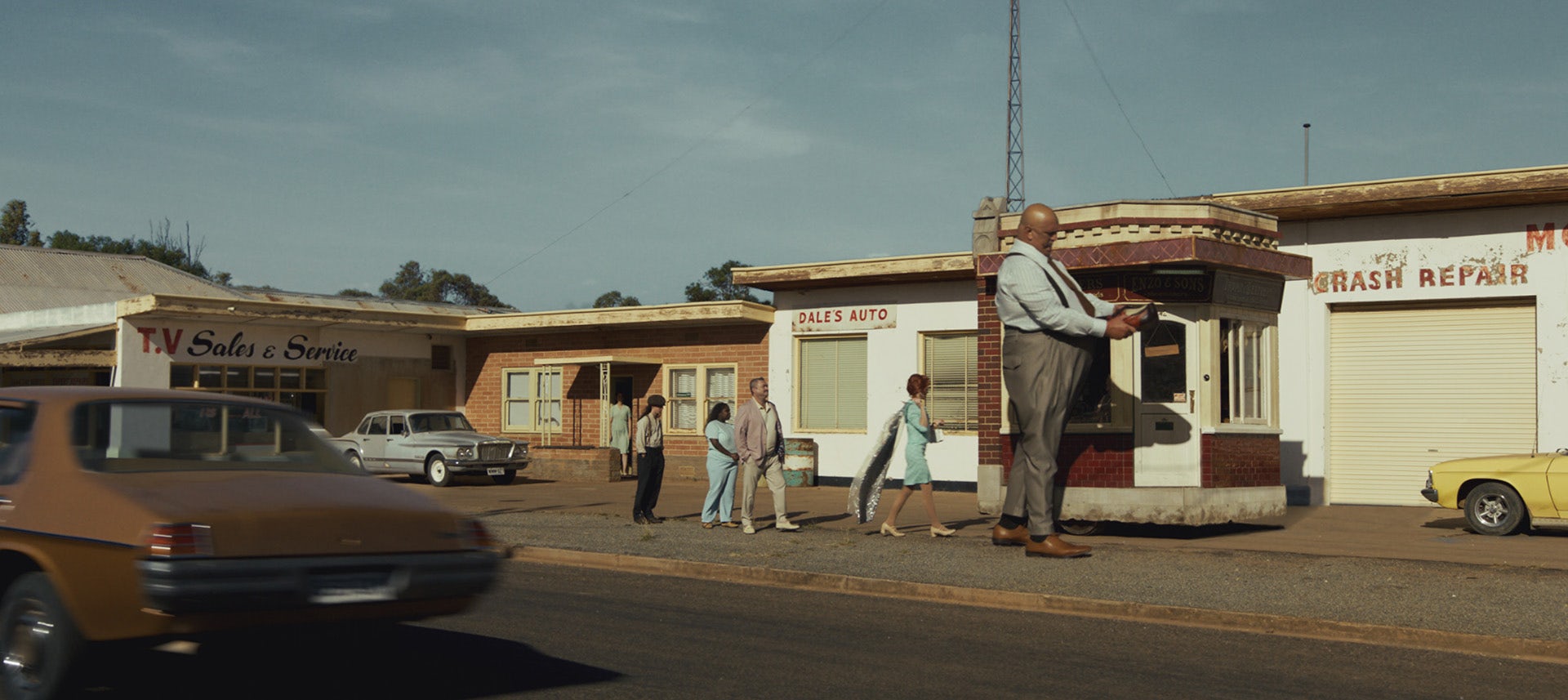 Still from a Telstra Business ad featuring people queueing up outside a small repair shop including one person at the front who is more double the height of the rest