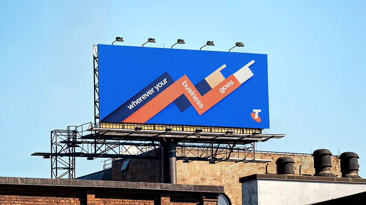Outdoor billboard for Telstra Business featuring an illustration of two interlinked arms pointing upwards and the tagline 'wherever your business goes'