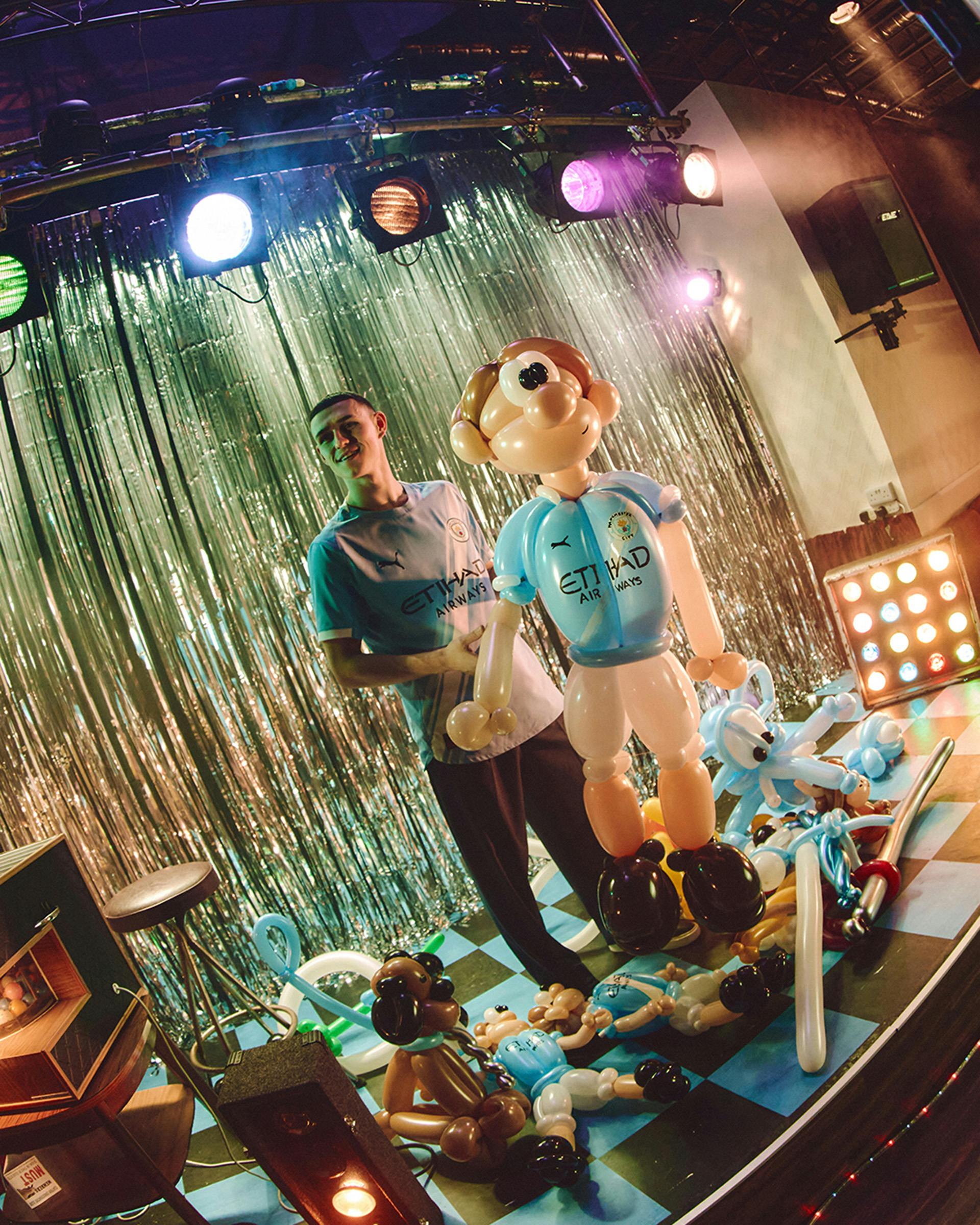 Still from Man City's 2025-2026 kit launch film featuring Phil Foden on stage holding a figure of a football made out of balloons