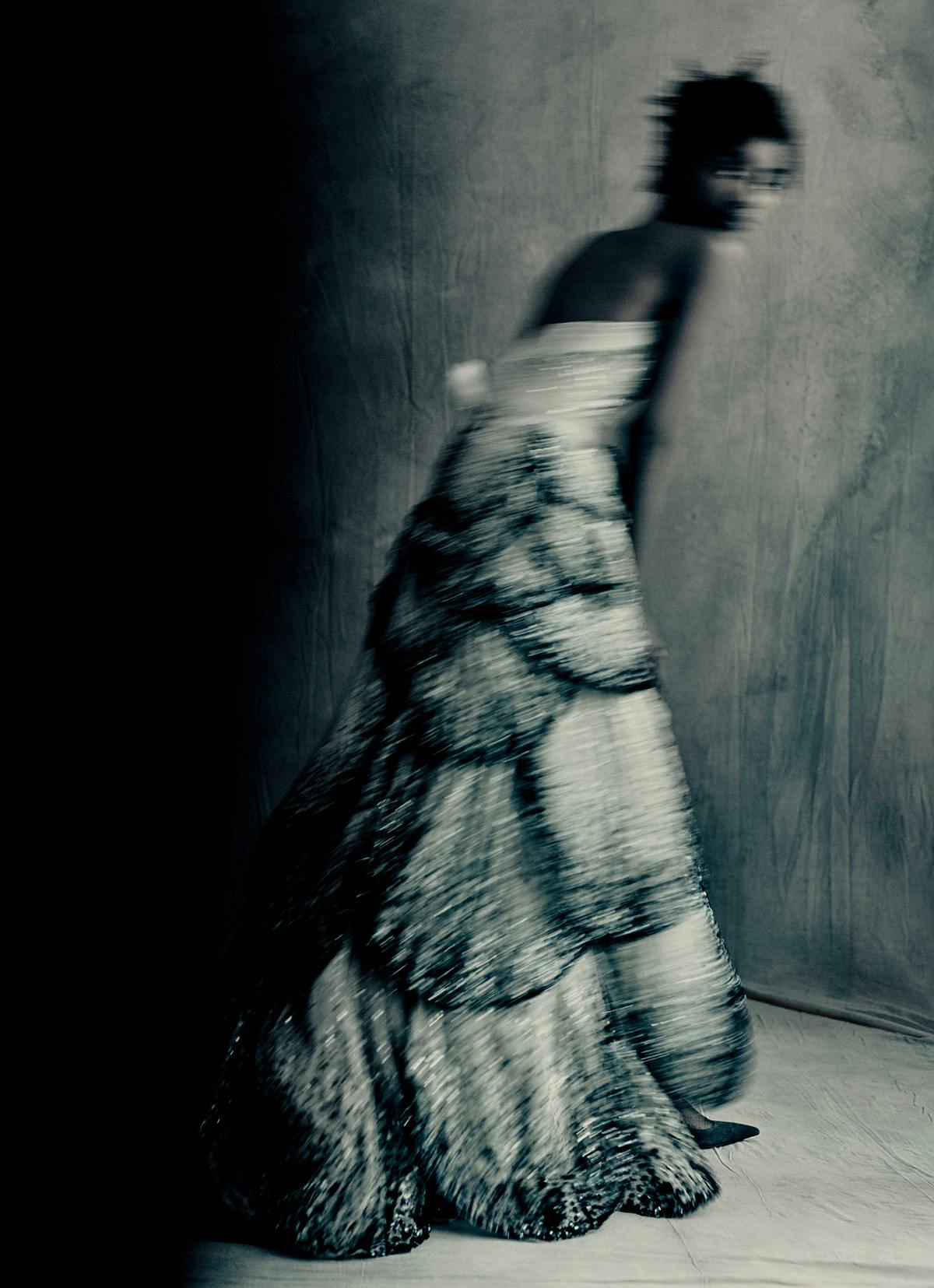 Blurred desaturated photo by Paolo Roversi of a model wearing a long tiered sleeveless dress