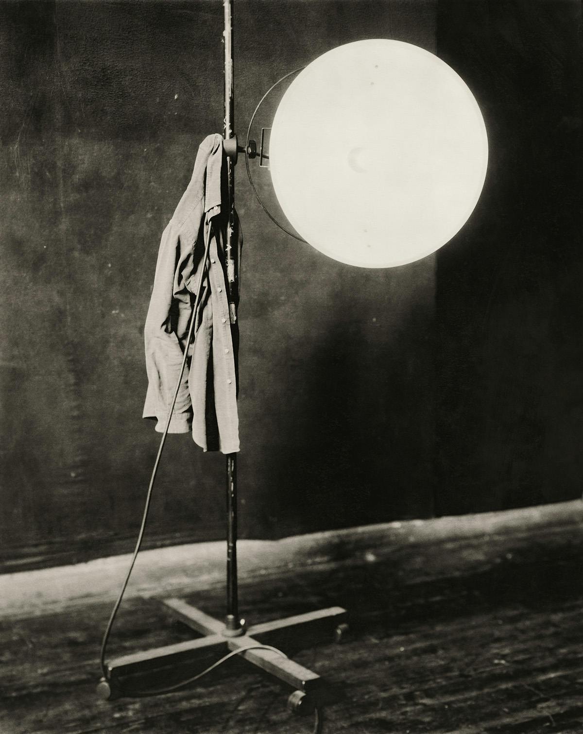 Desaturated photo by Paolo Roversi of a jacket hanging off a studio lighting rig with an illuminated bulb