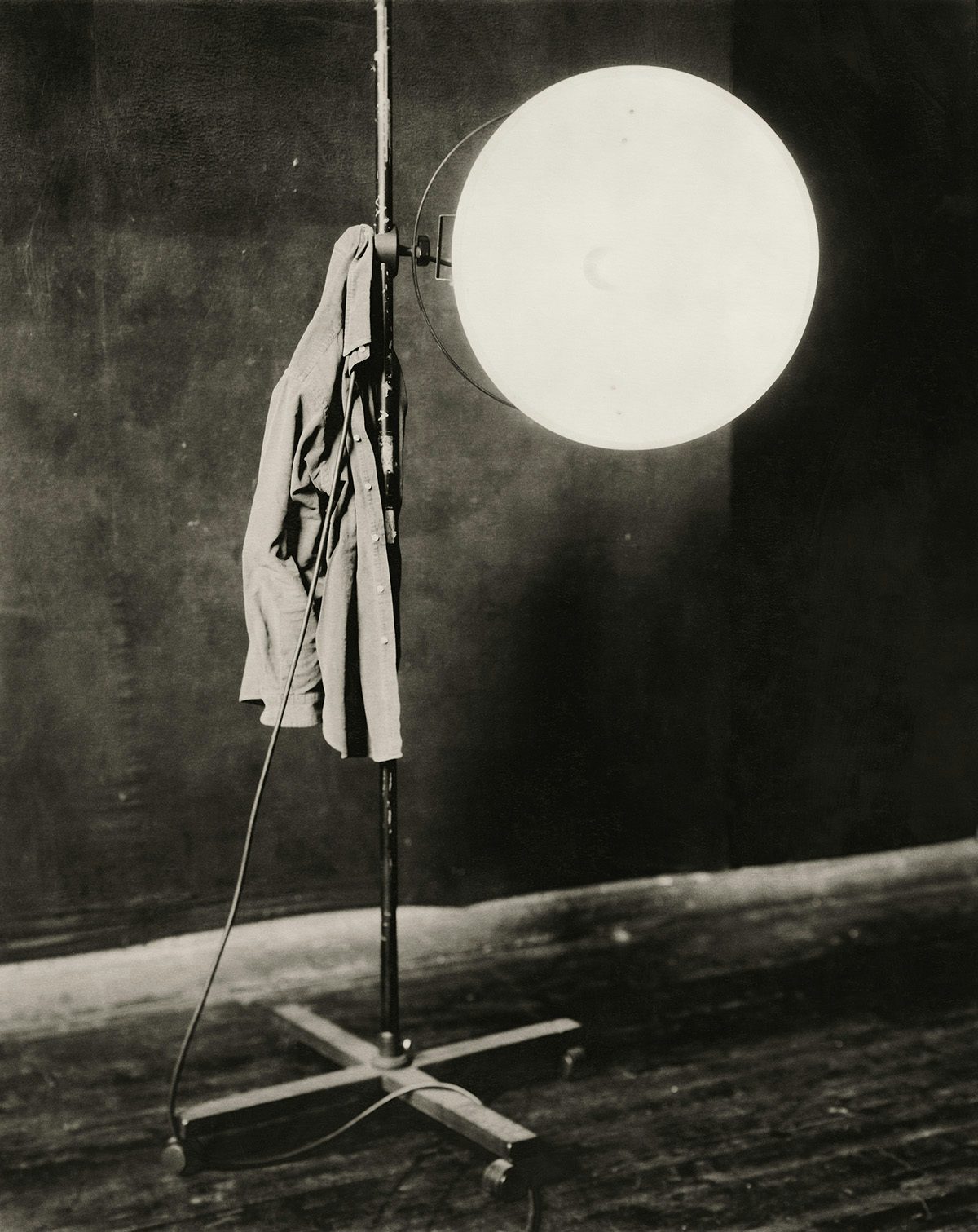 Desaturated photo by Paolo Roversi of a jacket hanging off a studio lighting rig with an illuminated bulb