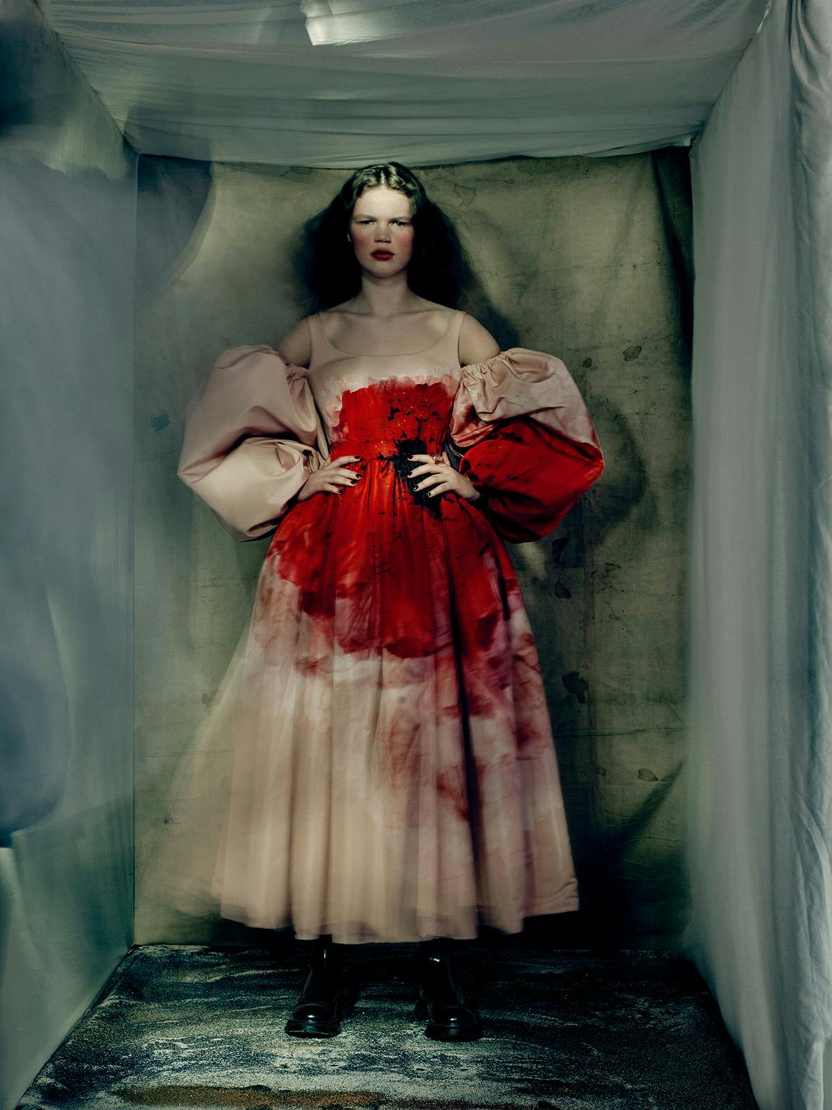 Studio photo by Paolo Roversi of a model wearing a pink puff-sleeved dress with a bright red mid-section resembling blood stains