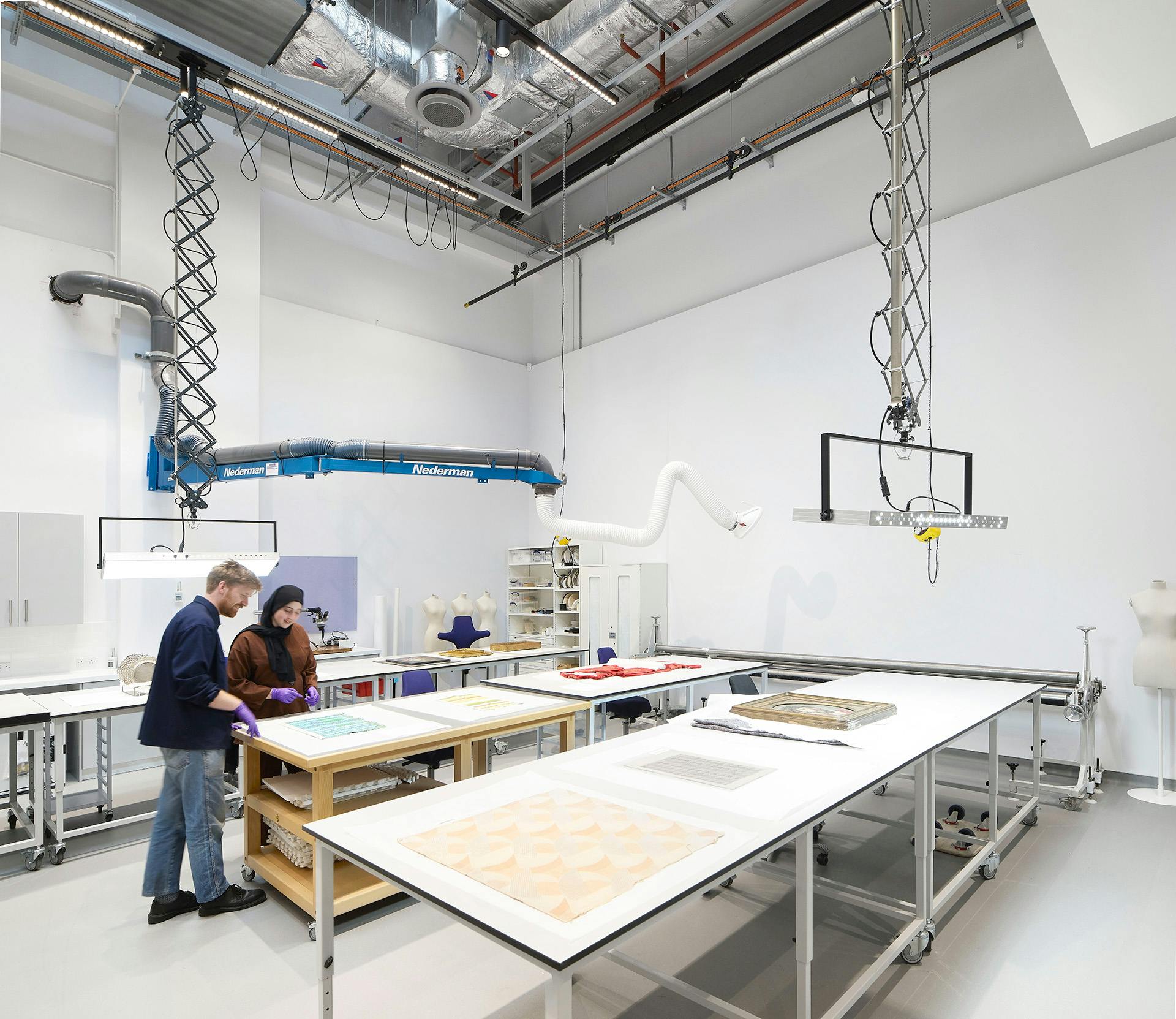 Two people standing over a conservation table in a studio in the V&A East Storehouse