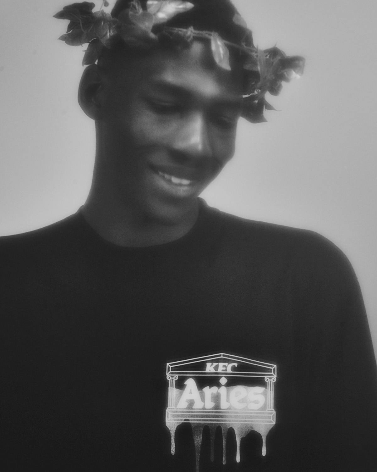 Black and white photo of a person wearing a laurel and a t-shirt with gravy appearance to drip from the Aries logo