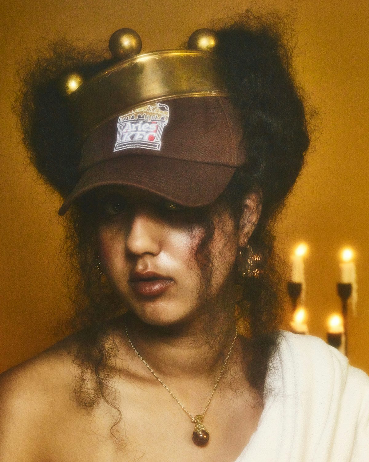 Soft focus photo of a person wearing a white robe and a brown Aries and KFC cap with a crown on top