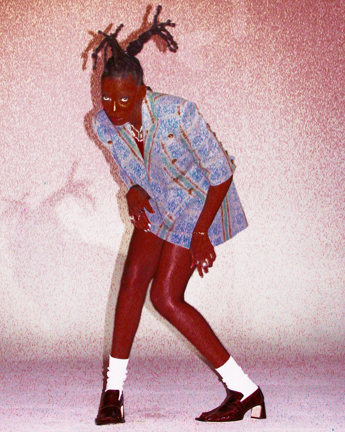 Oversaturated photo of Little Simz weather a thigh-length check jacket, white socks and heeled loafers by Thibaut Grevet