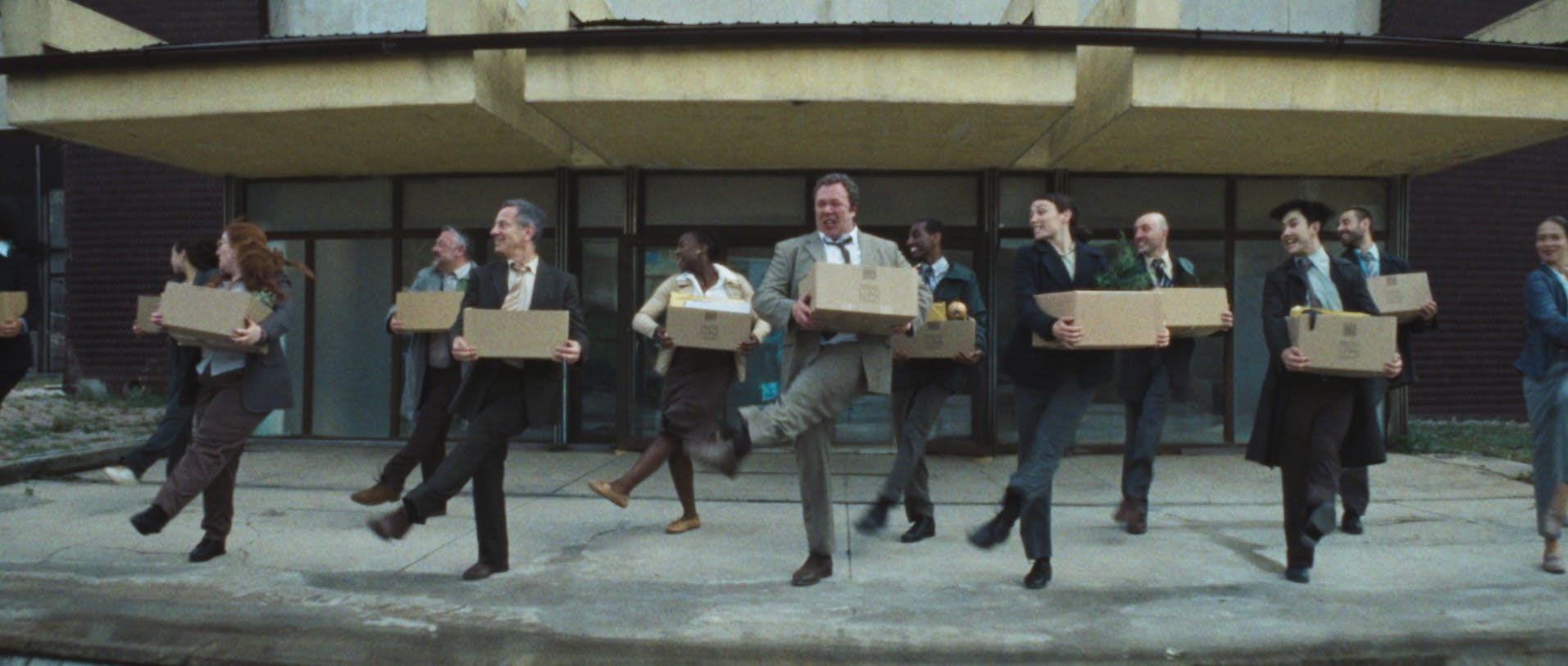 Still from Coinbase's ad showing a row of people in suits dancing while carrying boxes outside an office building