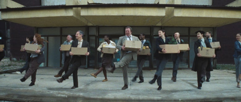 Still from Coinbase's ad showing a row of people in suits dancing while carrying boxes outside an office building