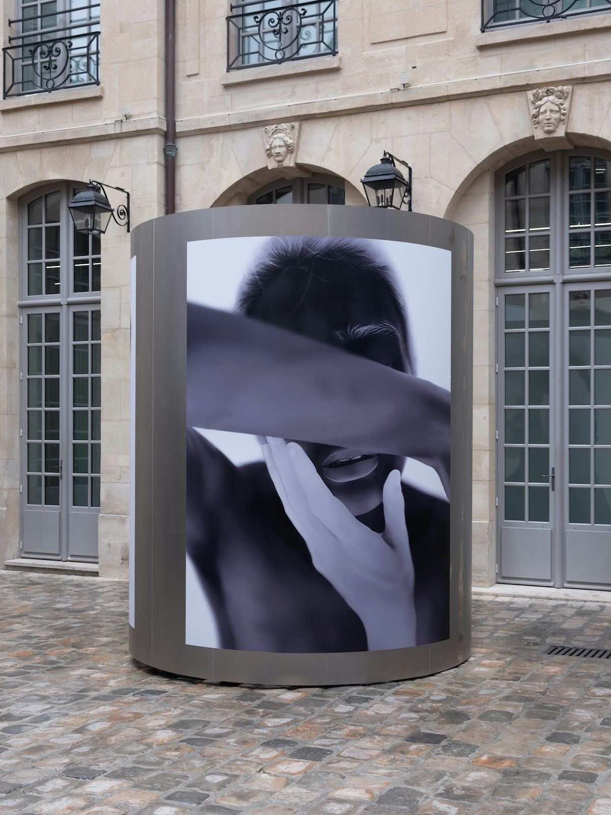 Thermal image of a person holding their own face by Yulia Mahr displayed on a pillar outside Dover Street Market Paris